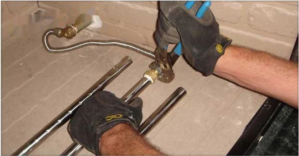 Gloved hands connecting the burner assembly on a gas log fireplace set